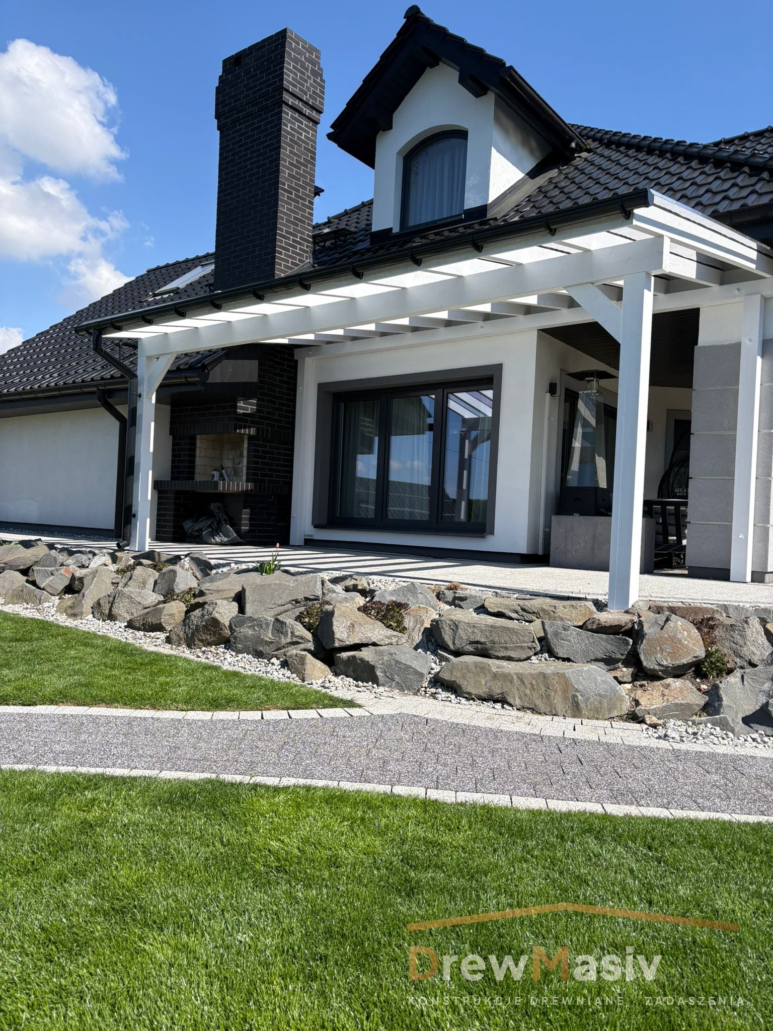 Biała pergola tarasowa DrewMasiv przy eleganckim domu z skalniakiem
